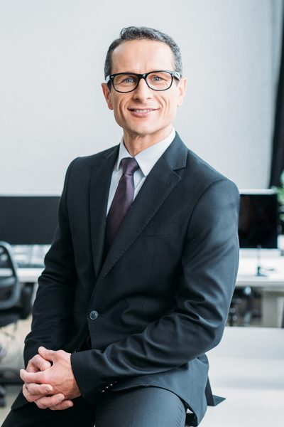 smiling-businessman-in-eyeglasses-sitting-on-table-V5AWVKC-rbbb2scgthwir9civuw9oenxt7sd0d40y5z9f69pio.webp